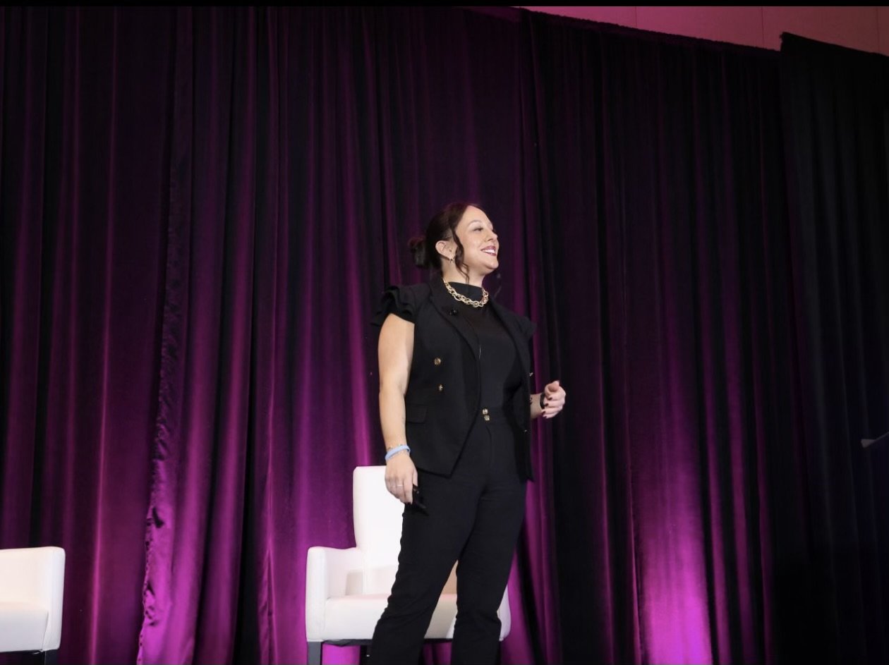 Steph Ketron smiling on stage in front of a magenta curtain